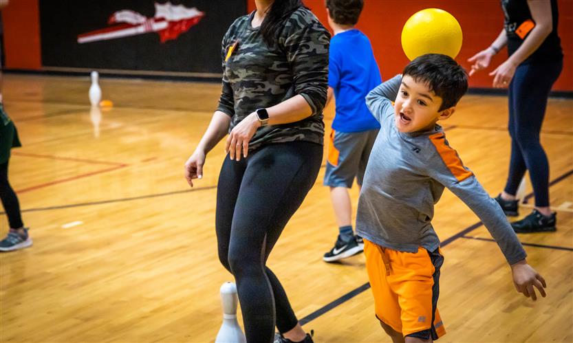 A boy wearing a grey shirt and orange shirts throws a ball during PE class
